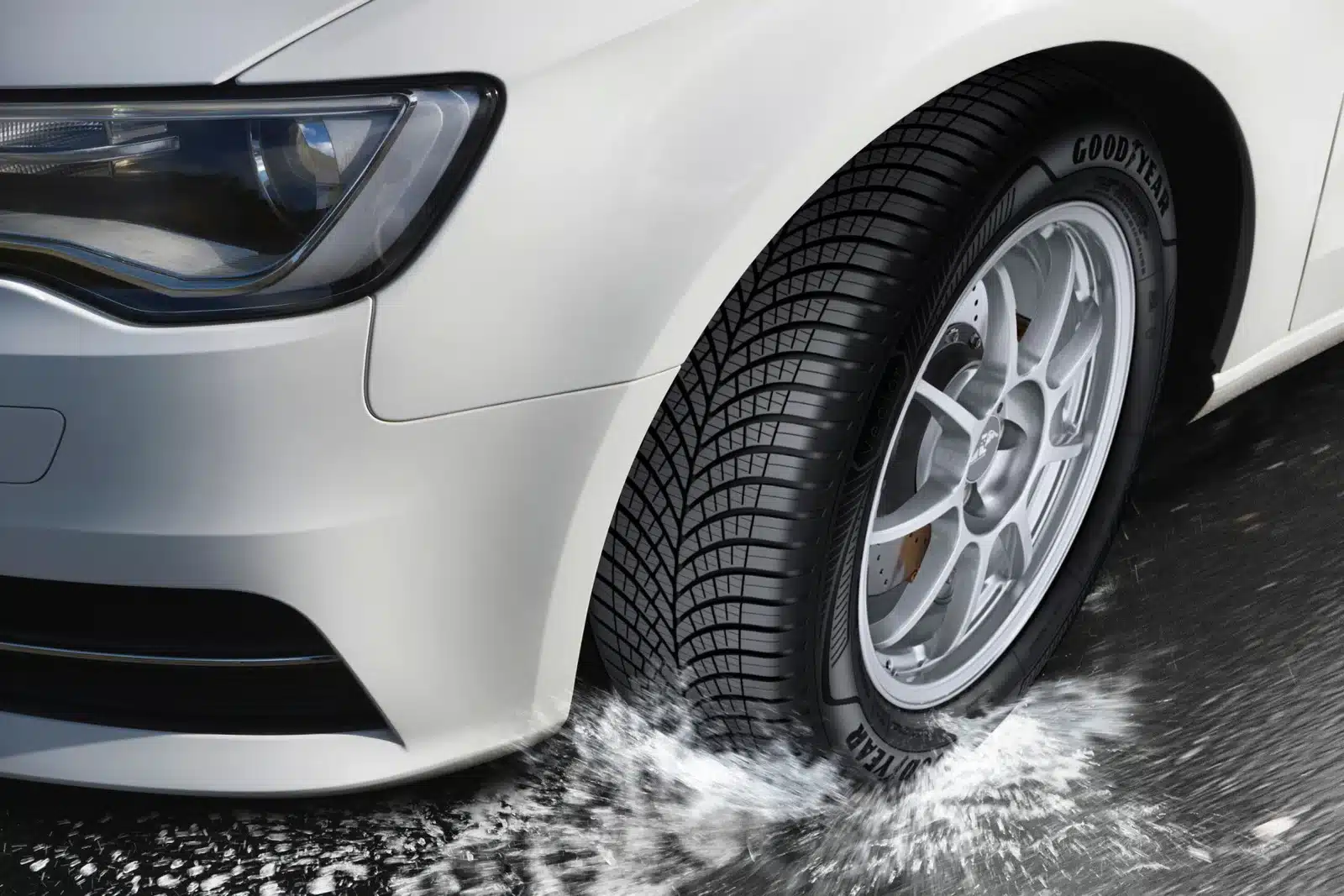 Witte auto met Goodyear Vector 4Seasons Gen-3 vierseizoenenband rijdt door een plas op nat wegdek